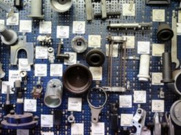 Das Bild zeigt eine Wand, die mit einem blauen Lochblech bedeckt ist, an dem verschiedene mechanische Bauteile und Werkzeuge befestigt sind.