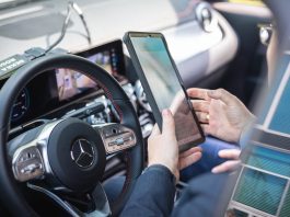 auf der Fahrerseite sitz jemand mit dem Handy in der Hand im Auto und prüft etwas am Auto mit einer Software.