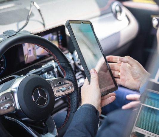 Mit neuem Garantielabel bringt BVfK gebrauchte Stromer zurück auf die Straße auf der Fahrerseite sitz jemand mit dem Handy in der Hand im Auto und prüft etwas am Auto mit einer Software.