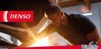 Ein Werkstattmitarbeiter arbeitet bei Tageslicht am geöffneten Motorraum eines Fahrzeugs. Die Szene vermittelt professionellen Klimaservice in einer modernen Kfz Werkstatt während der Sommersaison.