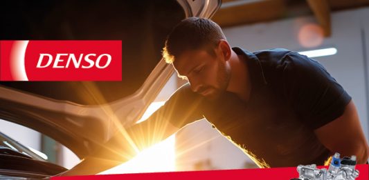 Ein Werkstattmitarbeiter arbeitet bei Tageslicht am geöffneten Motorraum eines Fahrzeugs. Die Szene vermittelt professionellen Klimaservice in einer modernen Kfz Werkstatt während der Sommersaison.